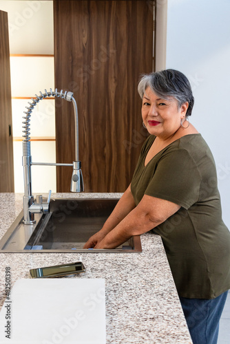 Senior woman with gray hair washing up in the kitchen