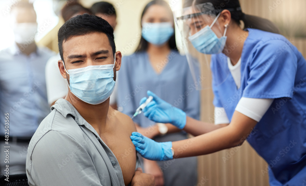 He doesn't like needles. Cropped shot of a handsome young businessman getting his covid vaccination from a female nurse in the office. He doesn't like needles. Cropped shot of a handsome young businessman getting his covid vaccination from a female nurse in the office.