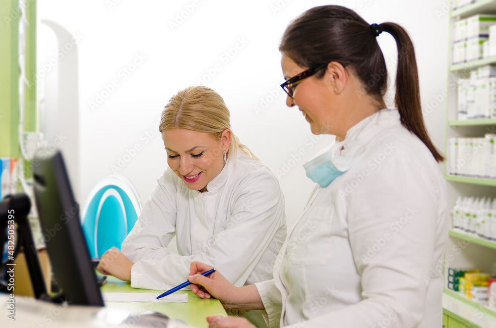 Fototapeta premium Pharmacist coworkers taking about prescriptions at work and smiling. Focus on woman in the back 