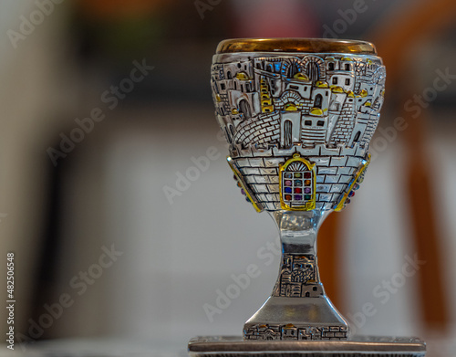 Traditional, decorative Jewish kiddush cup. Silver cup with saucer filled on a blurred background photo