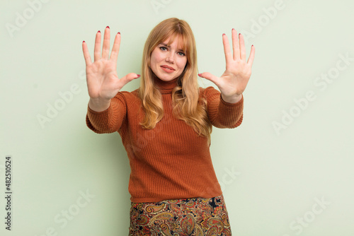 redhead pretty woman smiling and looking friendly, showing number ten or tenth with hand forward, counting down