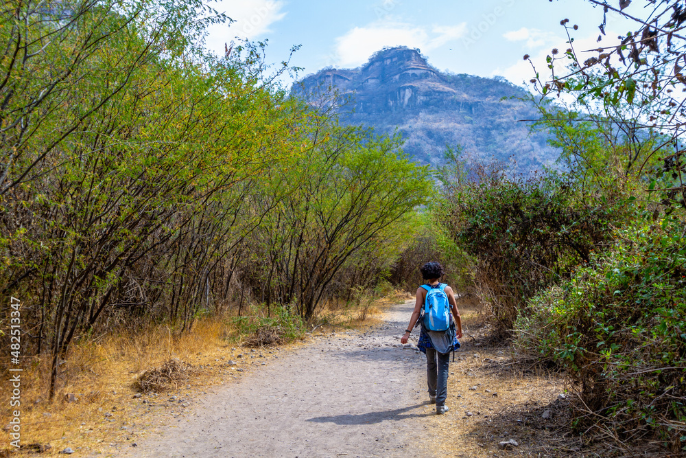 A woman walks through an outdoors path in the nature towards a mountain in the horizon in Huentitan, Jalisco in Mexico