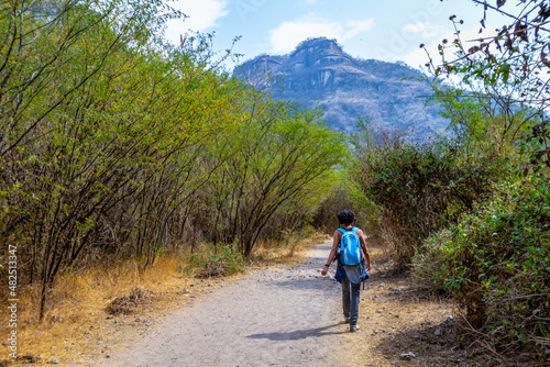 A woman walks through an outdoors path in the nature towards a mountain in the horizon in Huentitan, Jalisco in Mexico