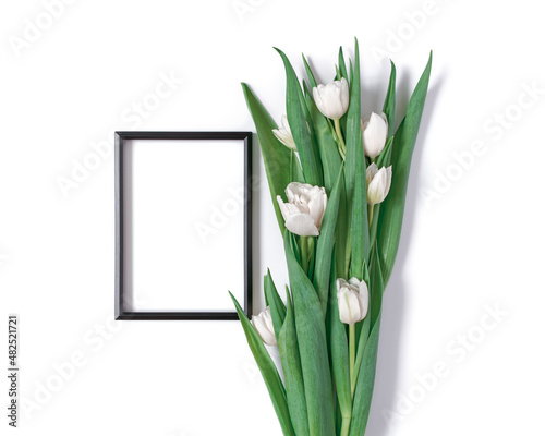 A bouquet of white tulips and a black blank photo frame are on a white background. Floral template with copy space from a bunch of fresh tulips. Flat lay  top view.