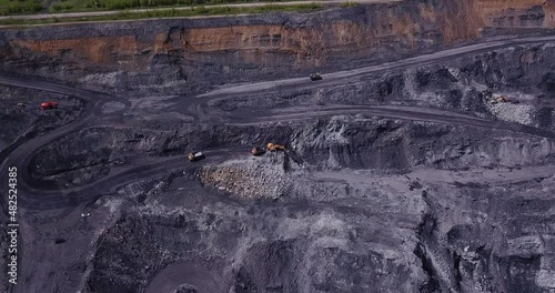 Aerial view of process of mining coal in a quarry. Drone flying above yellow dump trucks and mine excavators at coal mining area.