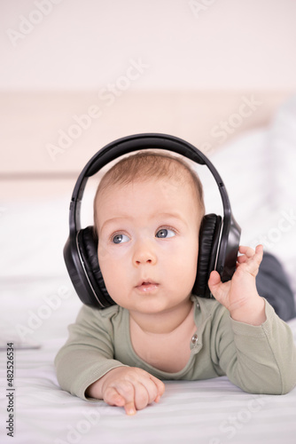 positive baby lying on a white background in headphones listening to music, infant 3 months old with headphones, young dj, happy carefree childhood