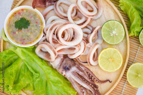 squid rings on wooden plate, Fresh squid cooked boiled with lettuce vegetable salad lemon and seafood sauce on table background