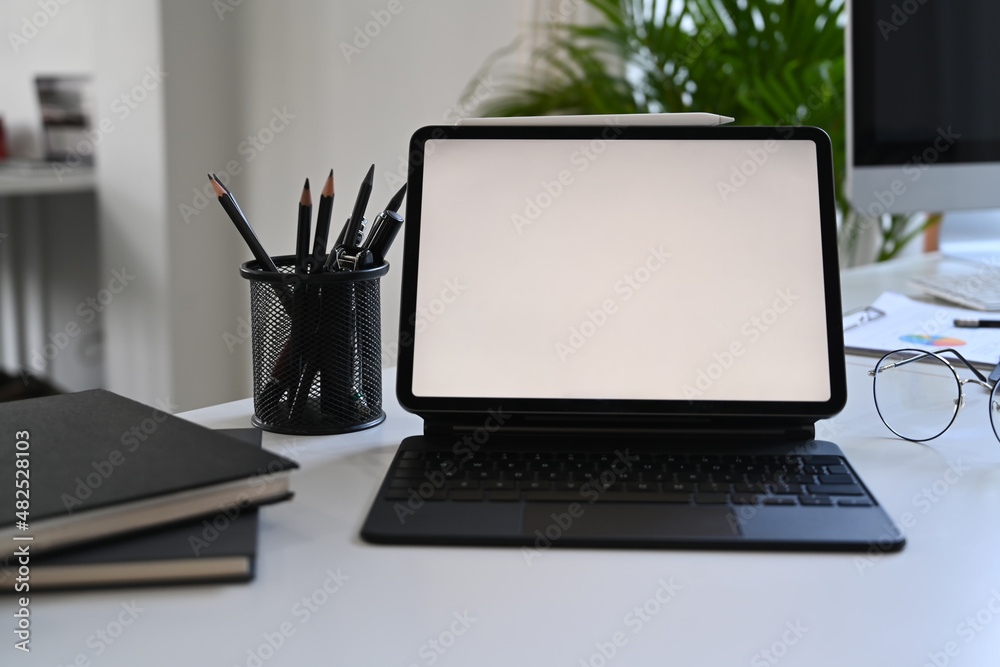 Fototapeta premium Computer tablet, notebooks, glasses and pencil holder on white office desk.