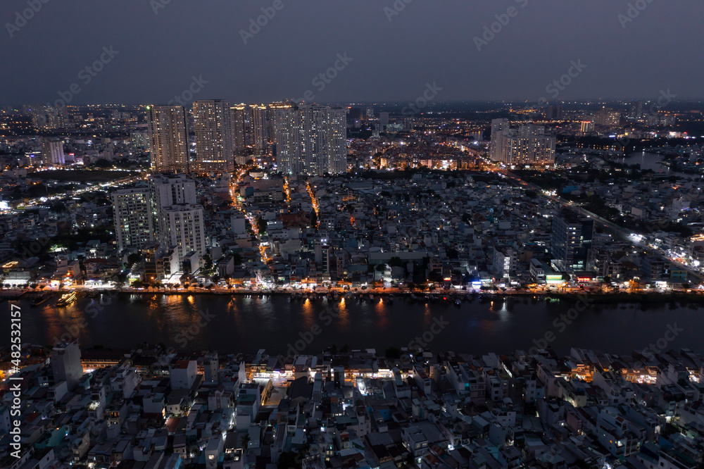 Panoramic view drone shot of Ho Chi Minh City in late evening looking across the Kenh Te canal with reflections and illuminated buildings.