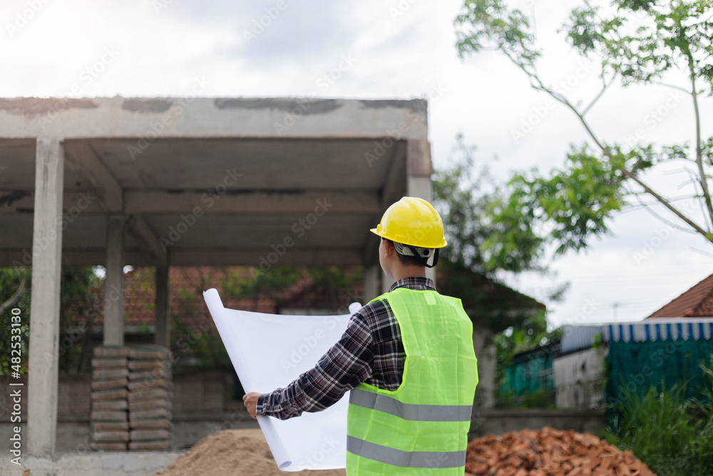 engineer concept The constructing manipulator who wears a hard yellow hat, dark-toned plaid blouse and soft green vest looking at the processing building construction