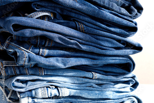 a pile of blue jeans on a white background. Sunlight. Close up (ID: 482538978)