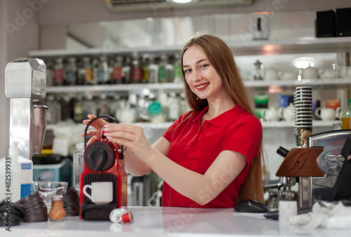 Young smiling woman barista making coffee in a coffee machine