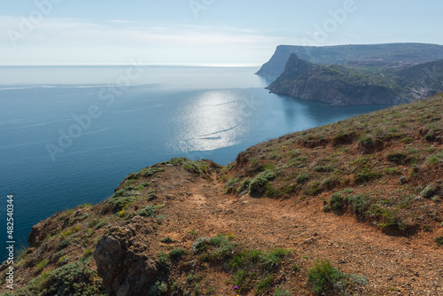 Mountains illuminated sea Balaclava. Light atmospheric spring landscape. View of high cliffs with green trees, blue sky, solar reflections. The concept of travel, active recreation, relaxation, walks