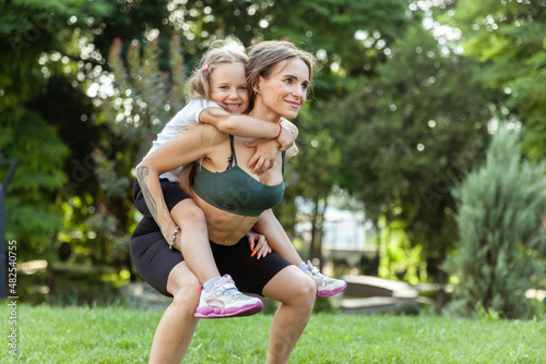 Athletic mom squatting with her little daughter outdoors, healthy lifestyle, fitness active family concept. Training together