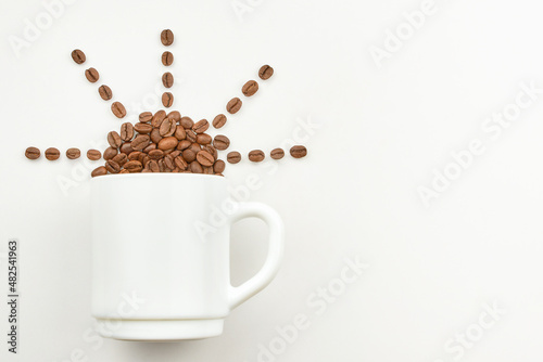 Cup and grains of coffee in the shape of the sun on a light background.