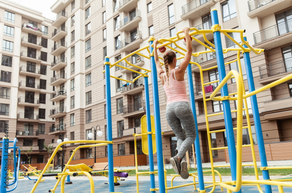 Fit woman pulls herself up on the outdoor playground. Active lifestyle