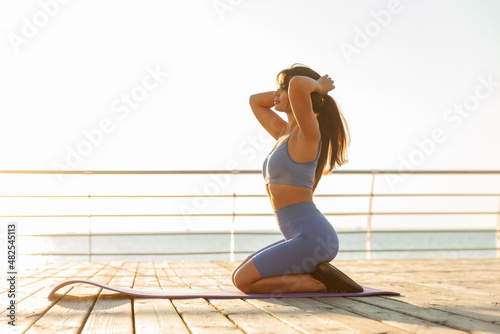 Foto Young fit woman sitting on a yoga mat on the beach and getting ready for a worko