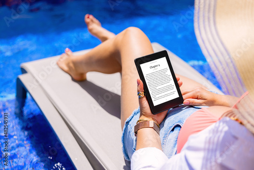 Woman holding e-reader device and reading e-book by the pool photo