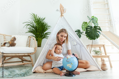 Mom with a little daughter sitting in a wigwam at home, studying the globe. Spend time together. Matyrdom concept photo