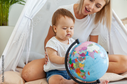 Mom with a little daughter sitting in a wigwam at home, studying the globe. Spend time together. Matyrdom concept photo