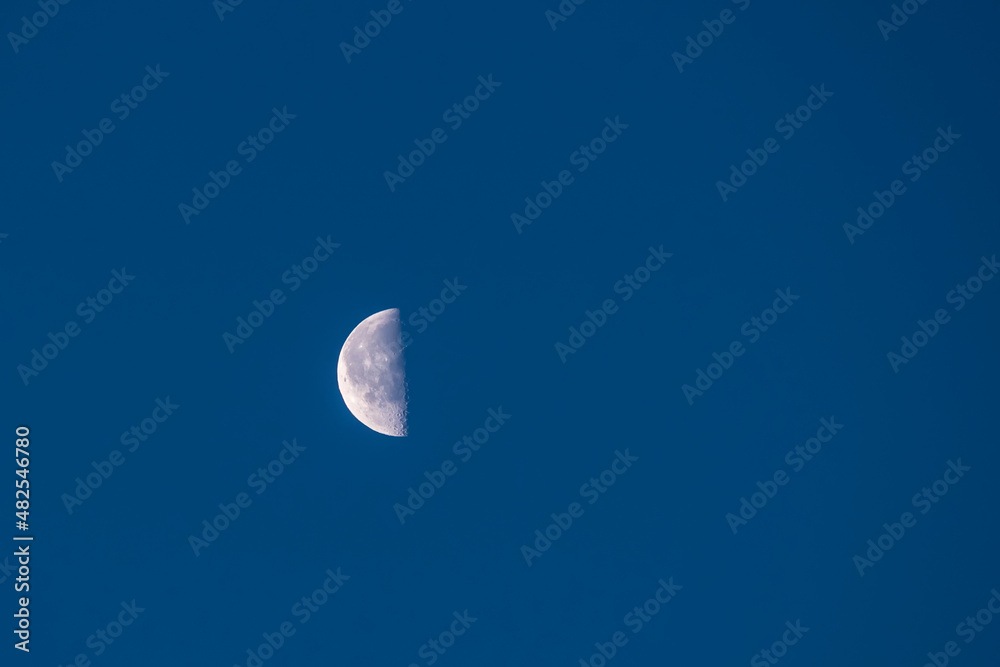 Half moon high against early morning cloudless blue sky Half moon high against early morning cloudless blue sky