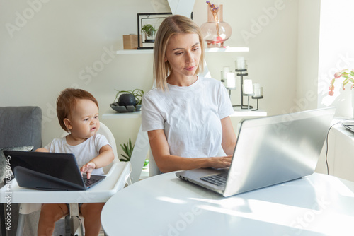 Mom and her little daughter use laptops and sit at the tables at home. Maternity, work and maternity