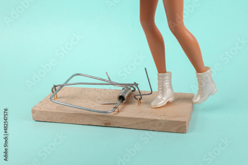 Minimal layout. Doll feet stepped into a mousetrap on a blue background. Deception, trap