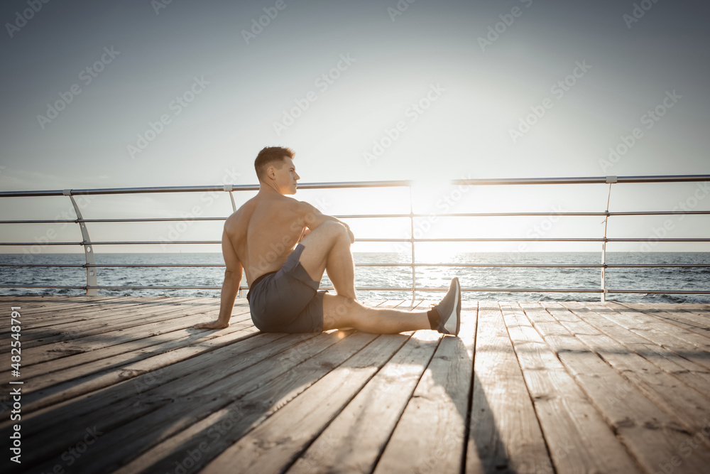 Muscular man practicing asana yoga poses for stretching muscles at sunrise on the beach