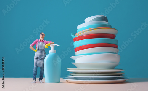 Happy woman standing next to a huge pile of clean dishes
