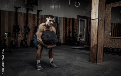 Muscular male athlete exercising with heavy bag in modern cross gym. Functional training