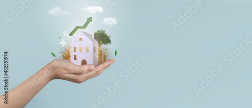 Real estate business investment and technology. Hand holding paper house with stack of bitcoin or gold coin and raising graph.Business investment and loans for real estate concept.