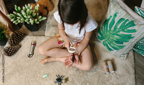 Top view of unrecognizable girl playing observing toy bugs with a magnifying glass
