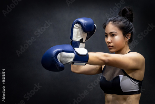 Young Asian woman boxer posing uppercut with blue boxing gloves in fitness gym. Female boxing class. Martial arts concept