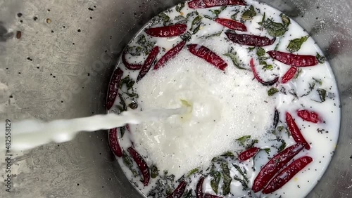 Pouring Milk Into Large Container With Herbs, Spices, And Chili Peppers. - vertical, high angle photo