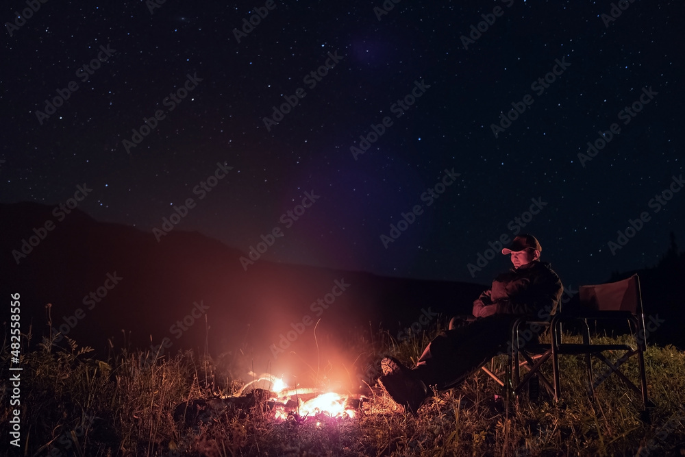 Man is resting near fireplace at night time with night sky Man is resting near fireplace at night time with night sky