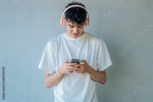 teen boy with mobile phone and headphones listening to music isolated on wall with copy-space © carballo