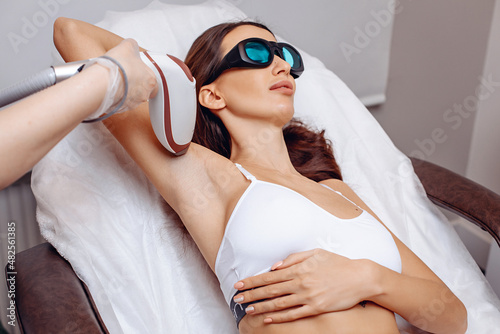 Providing high-quality beauty services in beauty salon. A young woman receives laser hair removal procedure for her armpits. Get result of smooth skin and no hair. The concept of beauty and grooming.