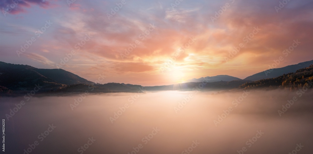 Sunset light among clouds above mountainous canyon in mist