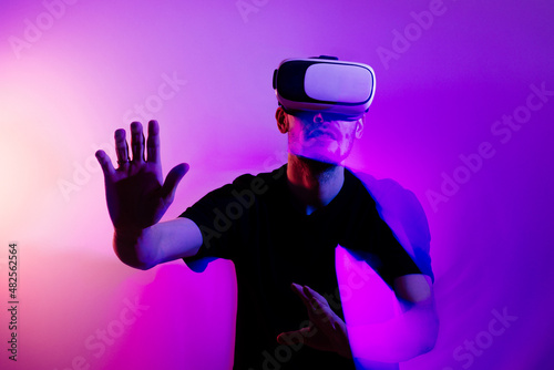Man using VR virtual reality glasses. Futuristic metaverse universe games and future in digital technology. Entreatment and NFT in neon colorful space. Happy male.  Video in 3d cyber space. © Girts