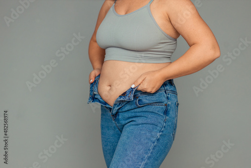 weight loss and overweight problem. a fat woman in a tank top and jeans is trying to button up or put on a size down jeans. disappointment from a non-athletic figure