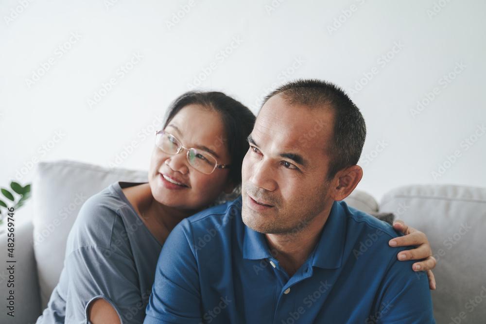 Portrait of Asian mature couple sitting in the living room. wife and husband hugging, holding hand with happiness and cheerful. Love, safety, and insurance family concept. Portrait of Asian mature couple sitting in the living room. wife and husband hugging, holding hand with happiness and cheerful. Love, safety, and insurance family concept.
