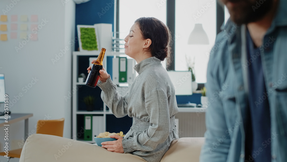 Portrait of woman with chips and bottle of beer after work, watching coworkers play game on foosball table. Person enjoying drinks and snacks to celebrate with fun activity after hours Portrait of woman with chips and bottle of beer after work, watching coworkers play game on foosball table. Person enjoying drinks and snacks to celebrate with fun activity after hours