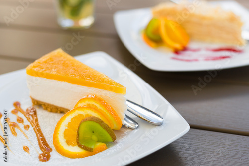 Slice of classic cheesecake with caramel topping. Pieces of cakeson ceramic white plate on wooden table in cafe. Food banner