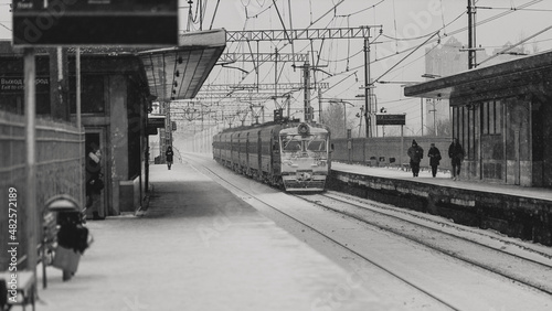 Commuter train departs from a snow-covered railway station in a snowfall. Black and white photography.