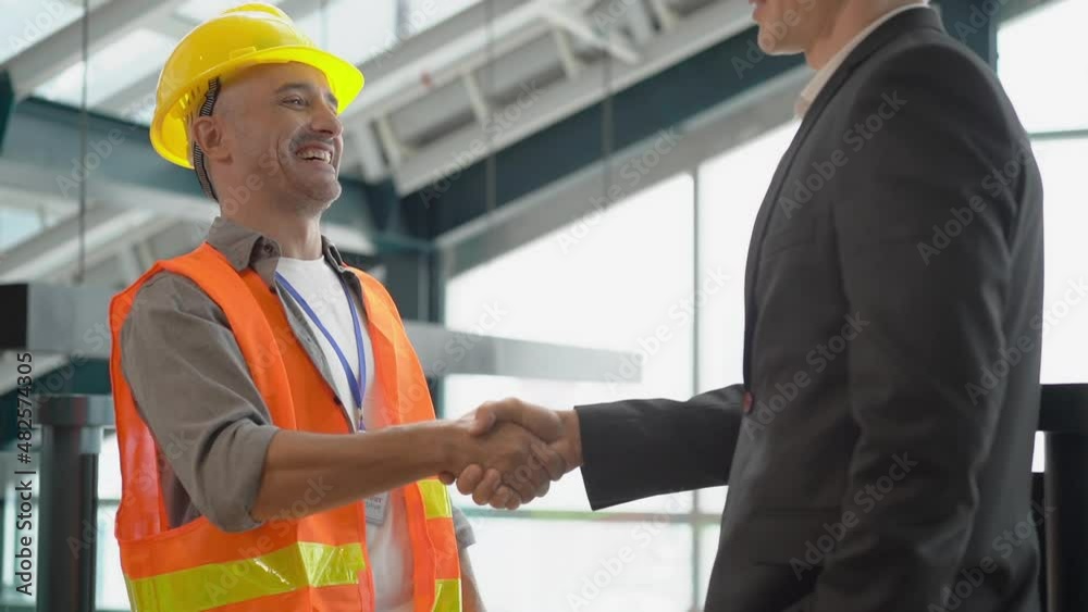 A happy middle-aged Latino male engineer in a reflective vest and helmet, smiling shaking hands and talking to a cropped view of young handsome Caucasian businessman in a suit at a construction site. A happy middle-aged Latino male engineer in a reflective vest and helmet, smiling shaking hands and talking to a cropped view of young handsome Caucasian businessman in a suit at a construction site.
