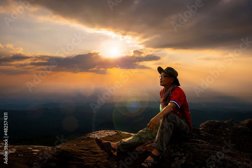 Tourists sit on strange shaped rocks and Colorful sunrise with Clouds over hill.Sun hiding behind a cloud on the day sky.Create a beautiful flare light concept.