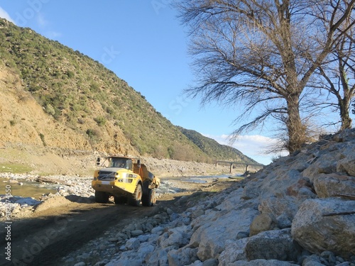 Engin de chantier de travaux camion benne et grue le long d'une berge rivière © Ourson+