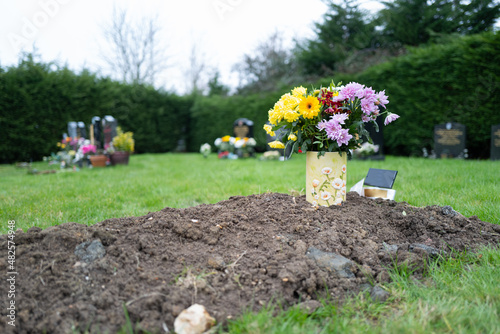 Vászonkép Shallow focus of a small bunch of pretty flowers seen on a freshly dug grave in a rural cemetery