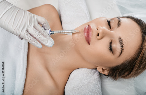 Woman while procedure lip augmentation at cosmetology clinic with beautician. Filler injection for beautiful female lips augmentation with hyaluronic, top view
