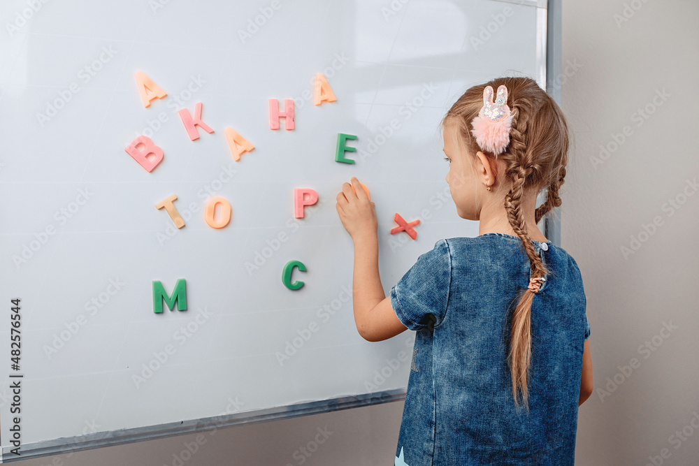 Portrait of a focused intelligent lovely kid standing in front of a white board with alphabet letters in the correct order. Focus concept